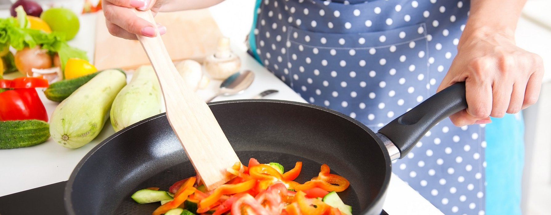 Rote Peperoni Streifen und grüne Zucchini Würfel werden in einer schwarzen Bratpfanne mit einem Holzspatel angebraten