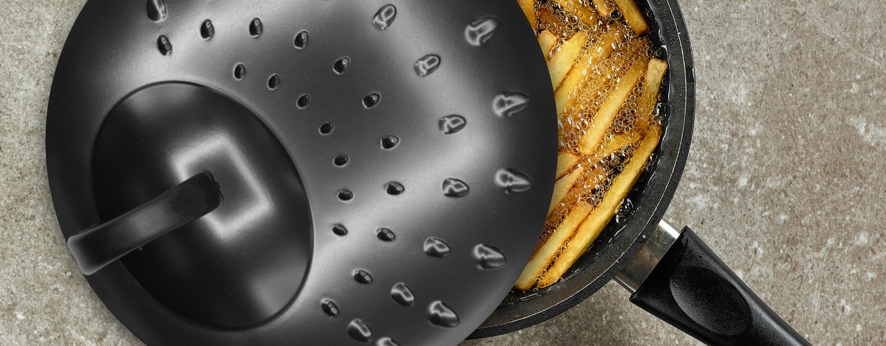 Schwarzer Pfannen-Spritzschutzdecekl auf einem Topf mit Pommes in heisem Öl