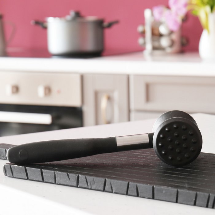 On a kitchen unit is a black cutting board and on that a black meat tenderizer