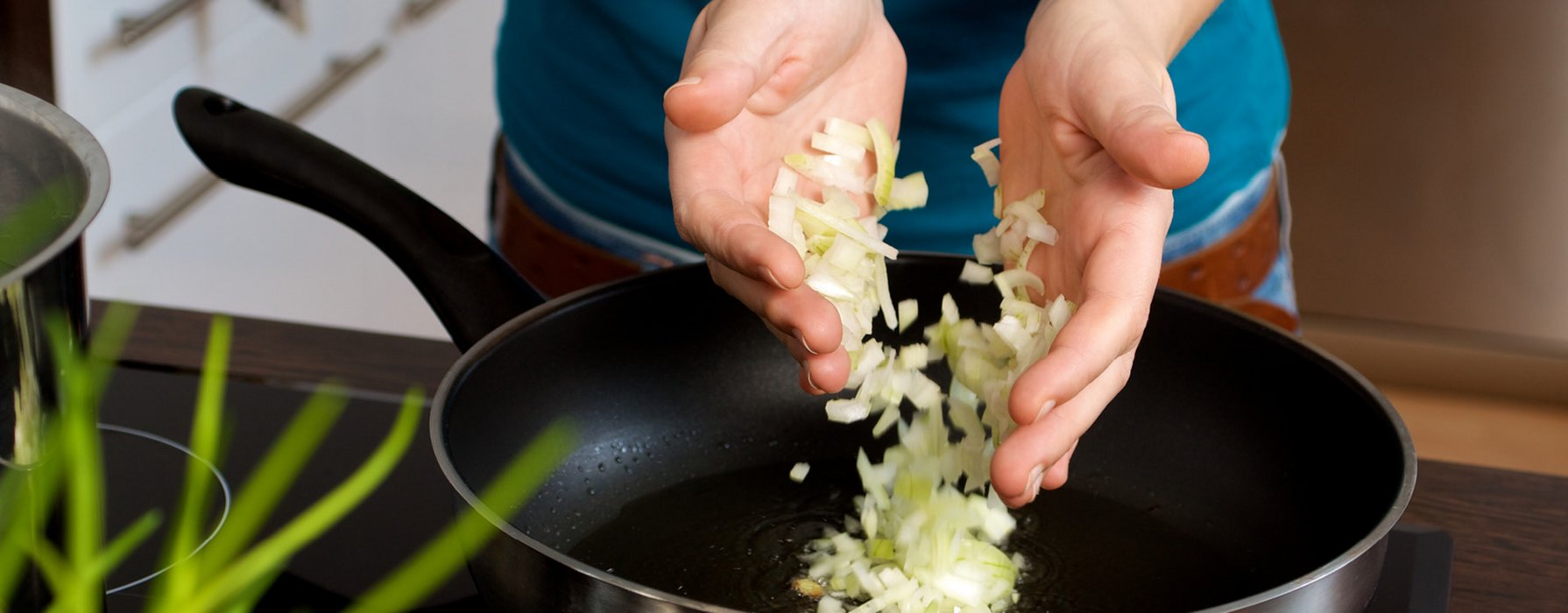 A handful chopped onions are thrown into a black coated wok