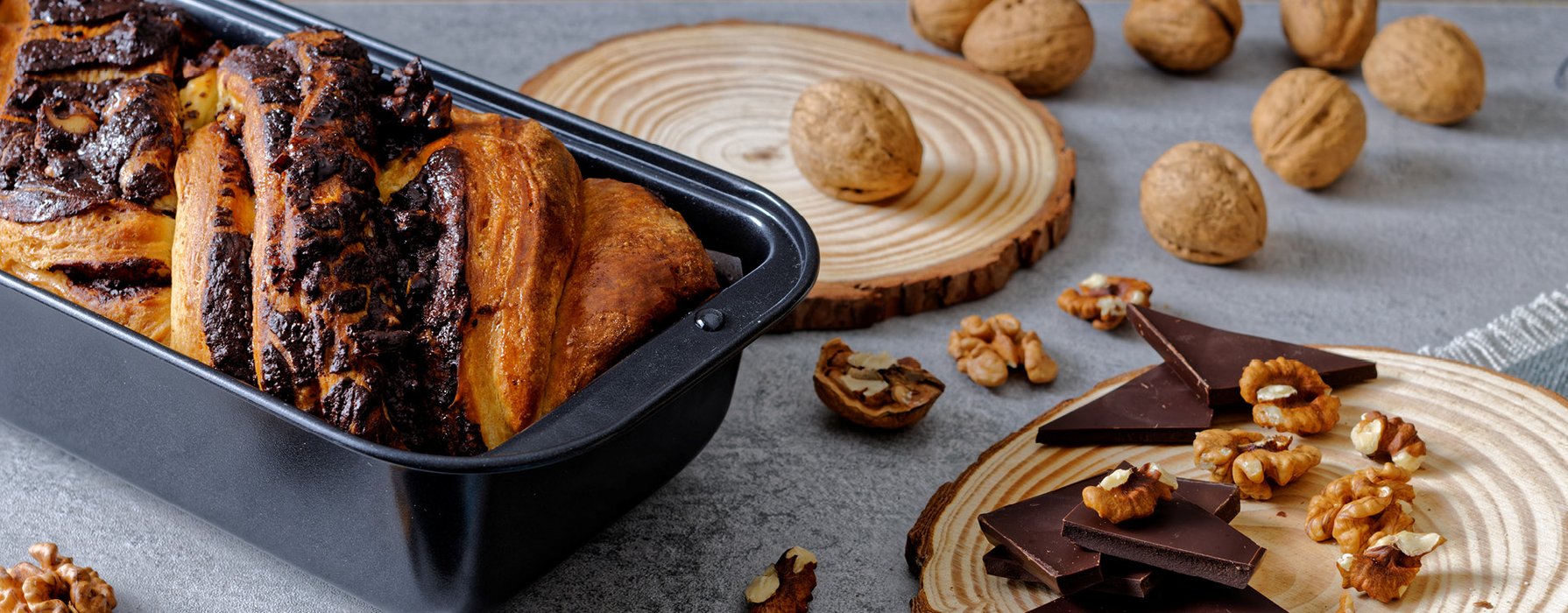 Baked nut cake in a coated loaf pan with some walnuts and chocolate chunks as a decoration by the side. 