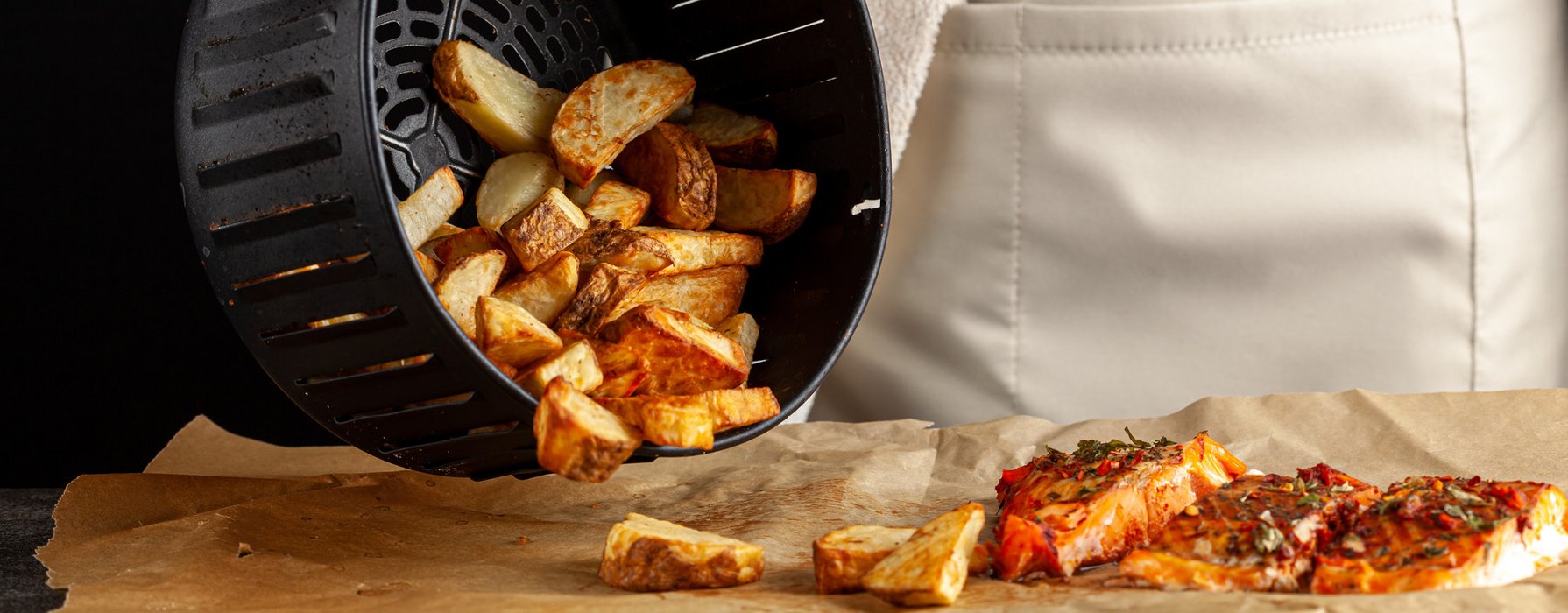  Baked potato slices are poured onto a piece of paper from a black coated basket of an airfryer