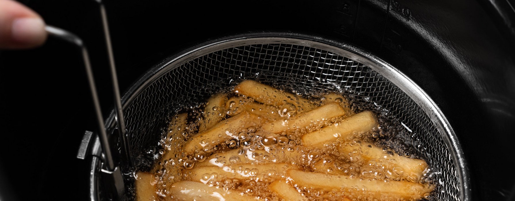 Pommes Frites werden in einem silbernen Korb in heissem Öl frittiert