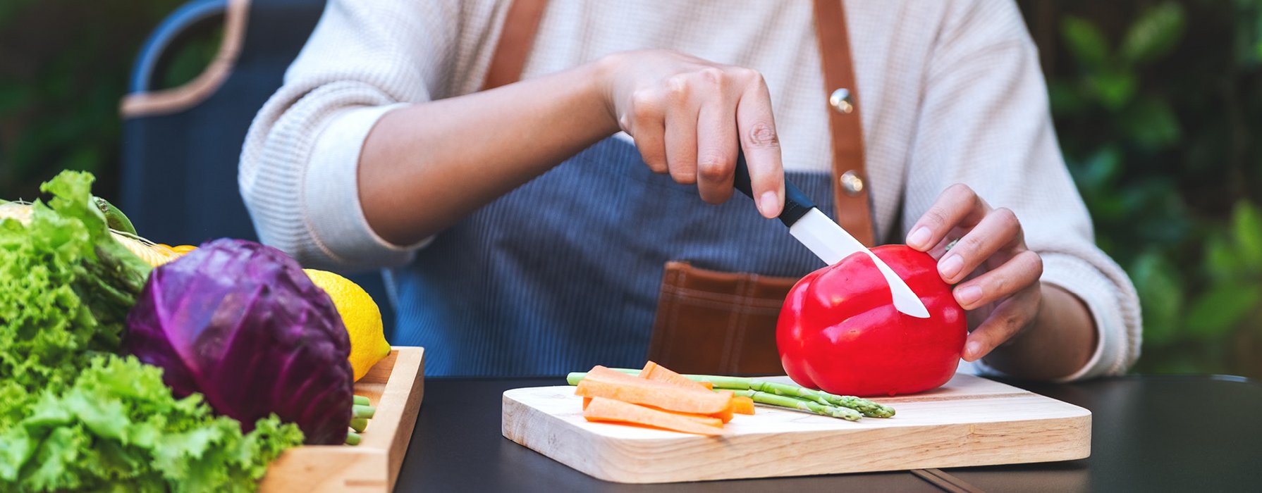 Frau schneidet mit einem Küchenmesser mit weisser Klinge eine rote Paprika in zwei Hälften