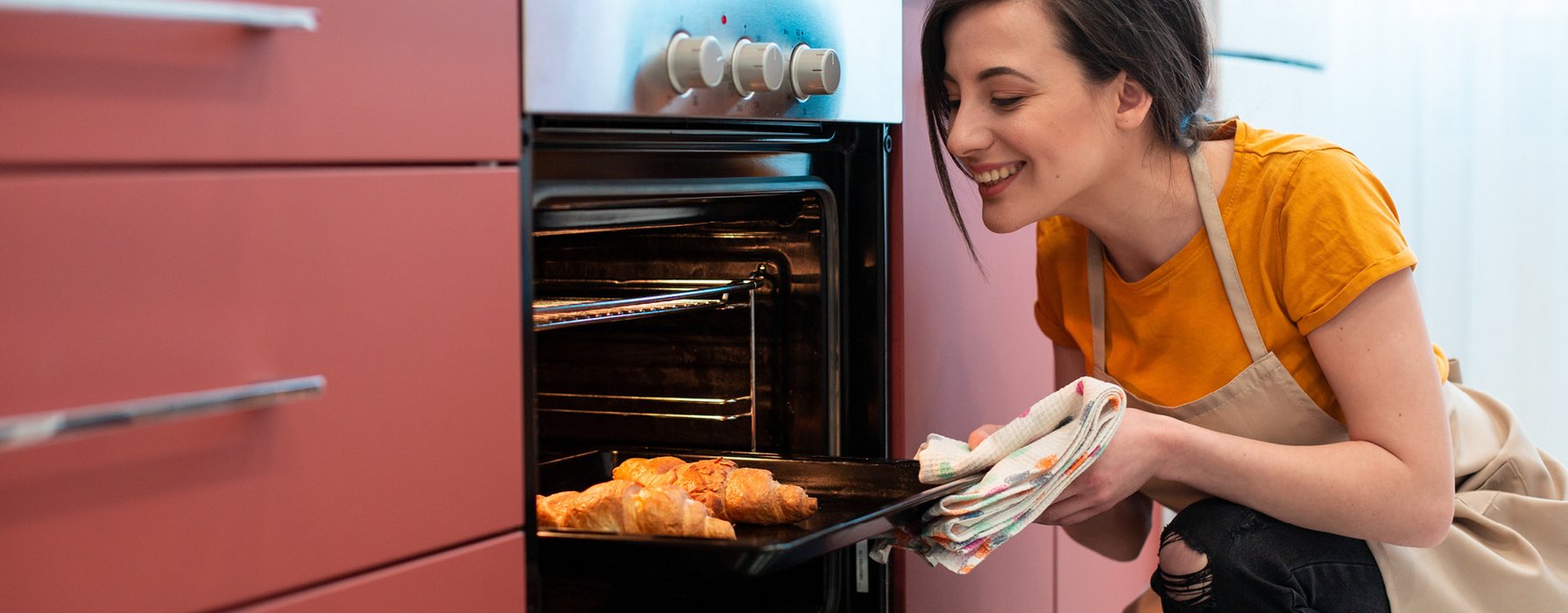 Woman is taking a baking tray with two nut croissants out of the oven. 