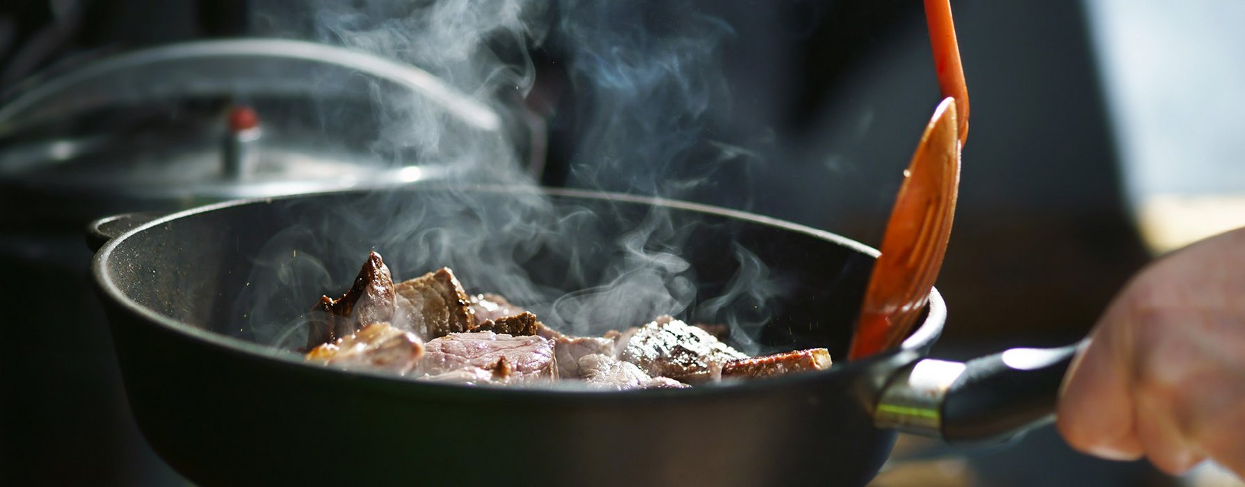 Steaming meat chunks are flipped in a black frying pan with a orange plastic trowel