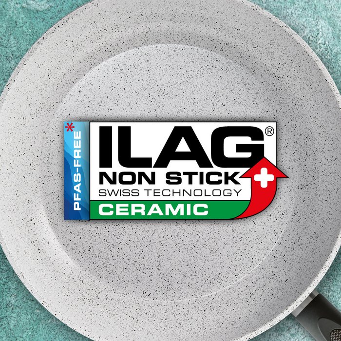 White inside of a frying pan with black fine sprinkles on it - ILAG logo with dark green shaded Ceramic lettering in the center and on the left hand side an extra labeling "PFAS-FREE" in blue 