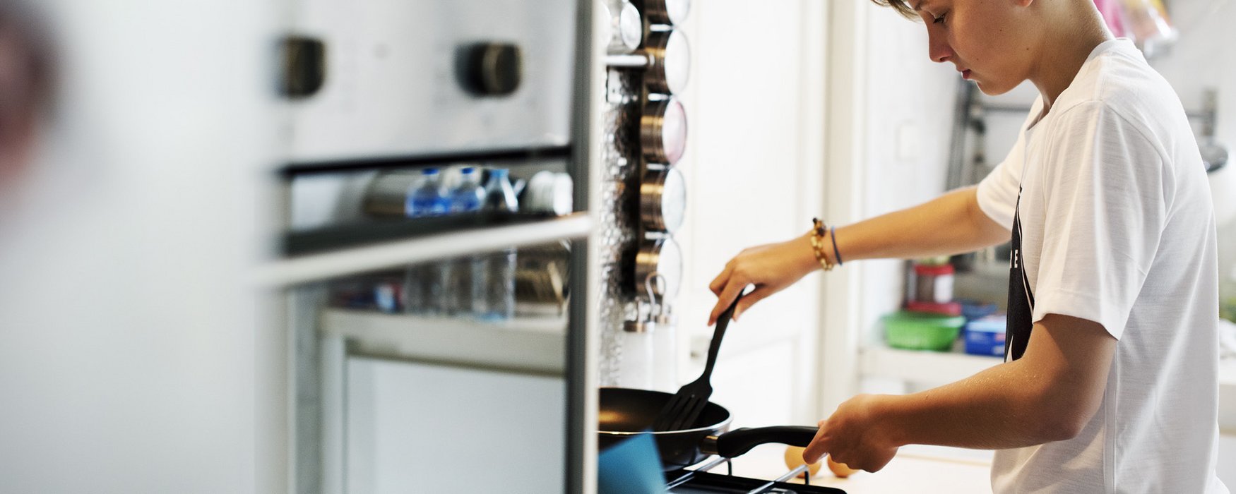 Teenager is turning food with a plastic trowel in a black frying pan