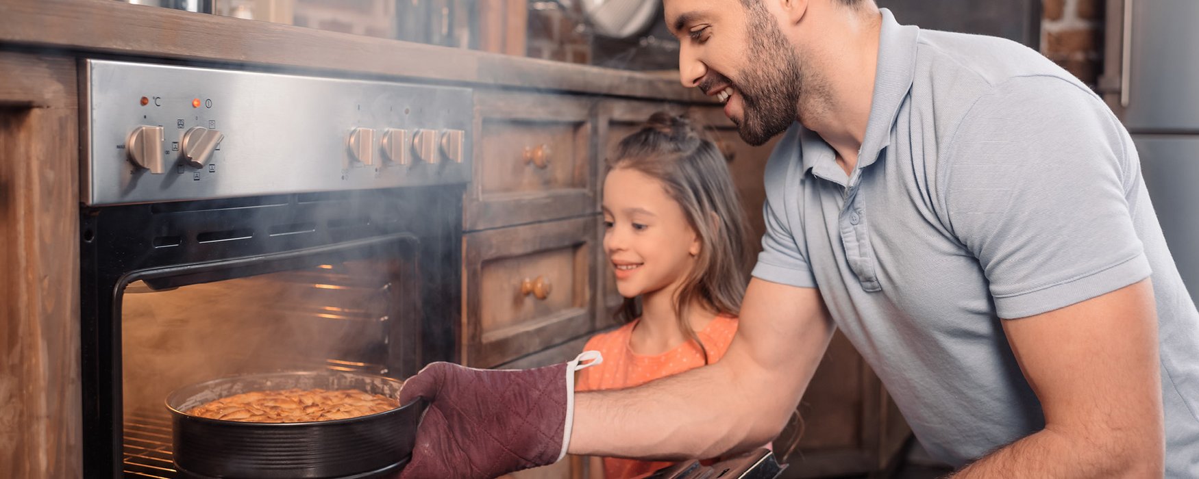 A man and a little girl are taking a baked cake out of the oven.