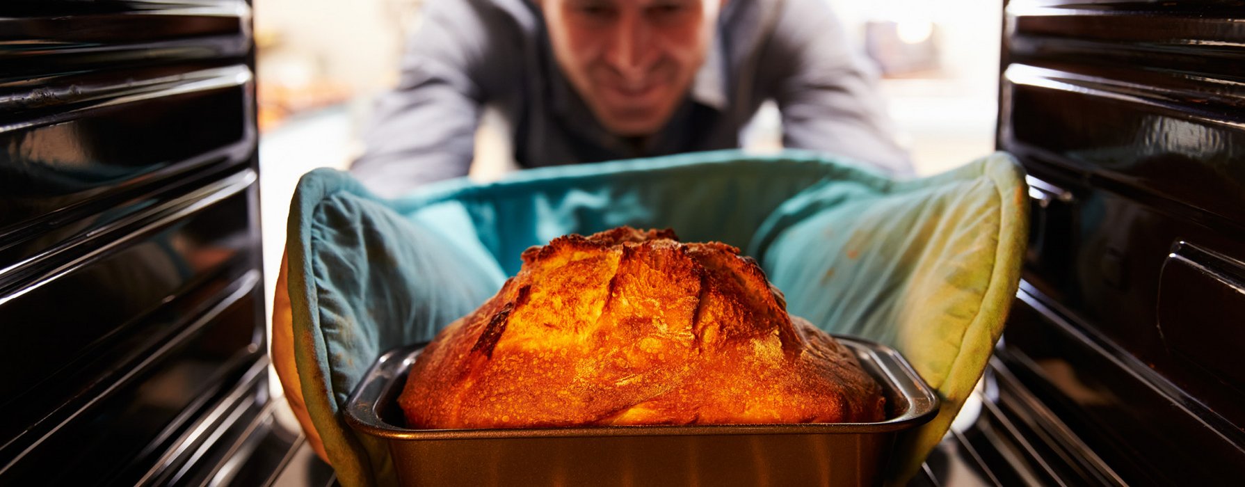 Junger Mann greift mit Handschuhen nach einer im Backofen liegenden Auflaufform, in der sich ein in Teig eingewickeltes Fleischstück befindet