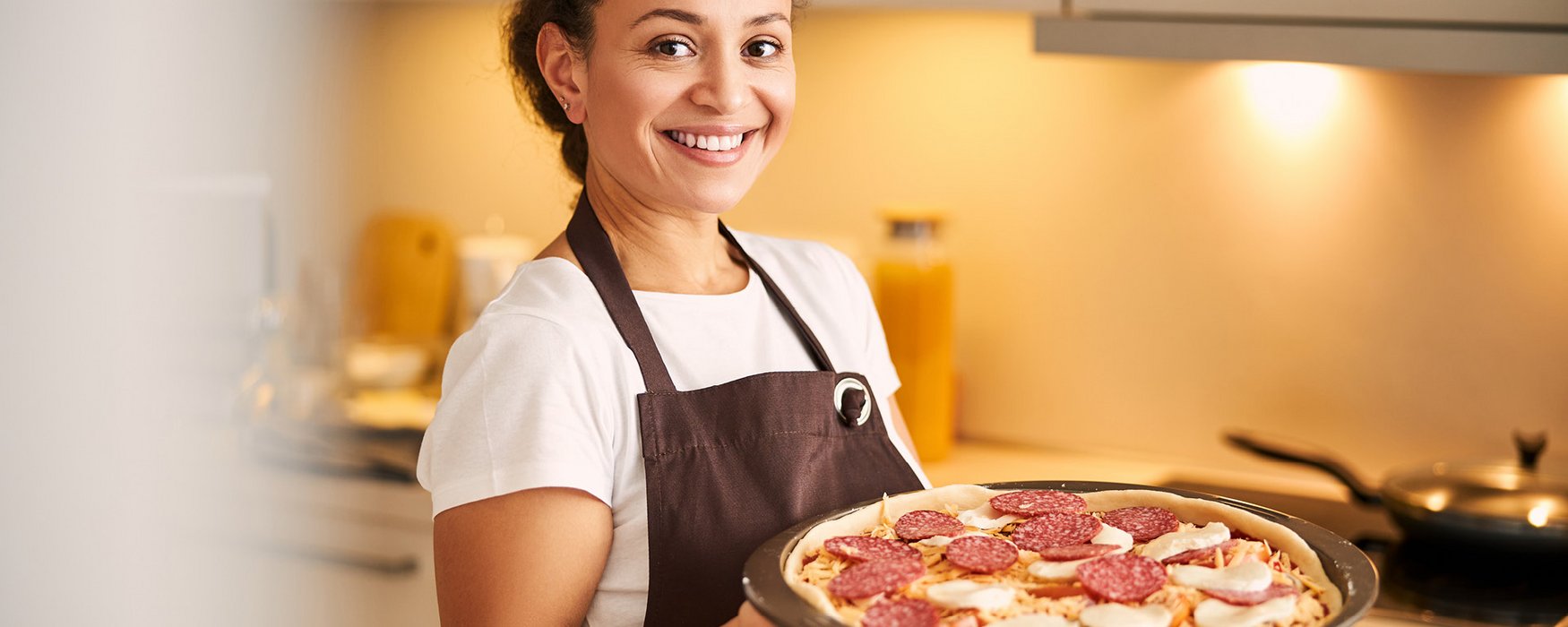 Junge Frau präsentiert eine Pizza auf einem Backblech, die gleich in den Ofen geschoben wird