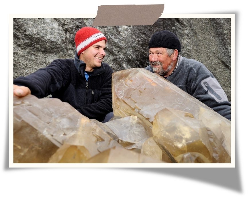 Two men are laughing while raw crystals are laying in front of them. 