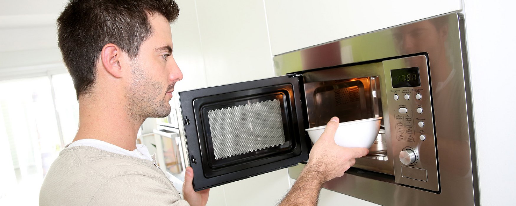 Young men is placing a white bowl into the microwave