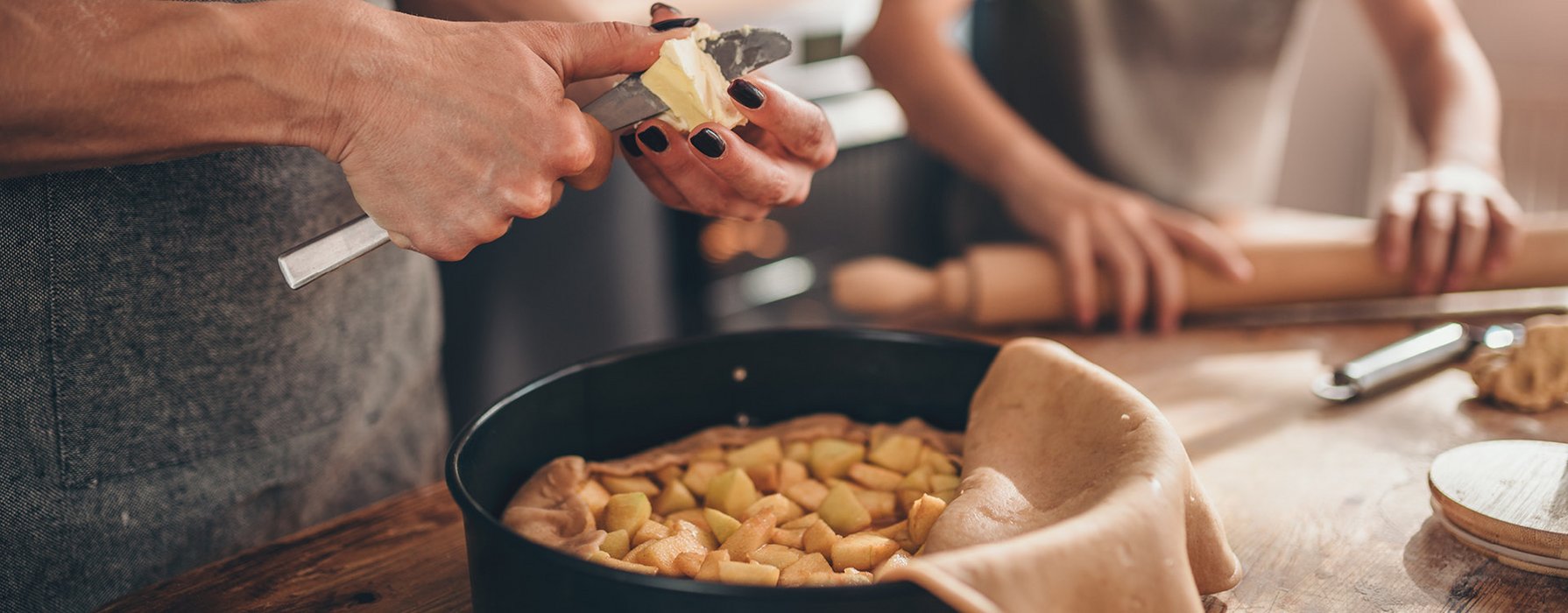 Frau schneidet Butterstücke um diese über den in einer runden beschichteten Backform zubereiteten Apfelkuchen zu verteilen