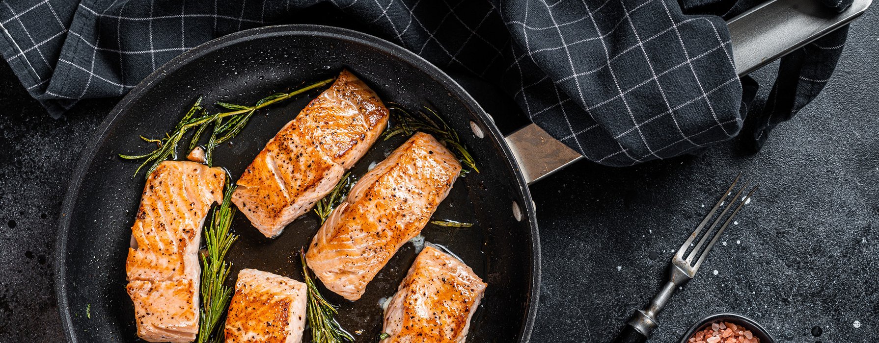 Five crispy roasted salmon chunks garnished with rosemary sprigs in a frying pan