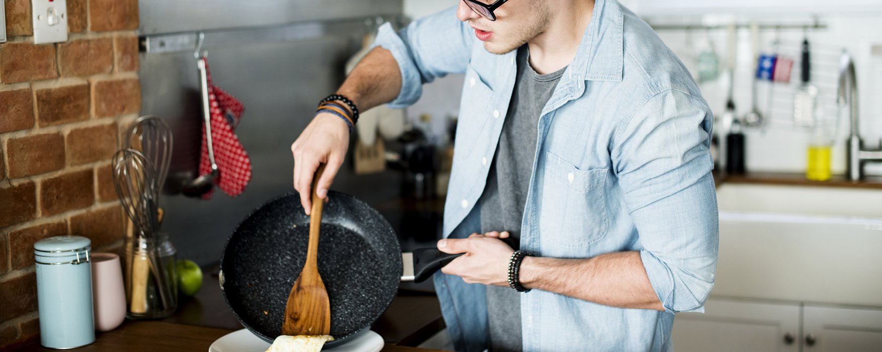 Young man scoops food with a wooden trowel out of a black marbled pan