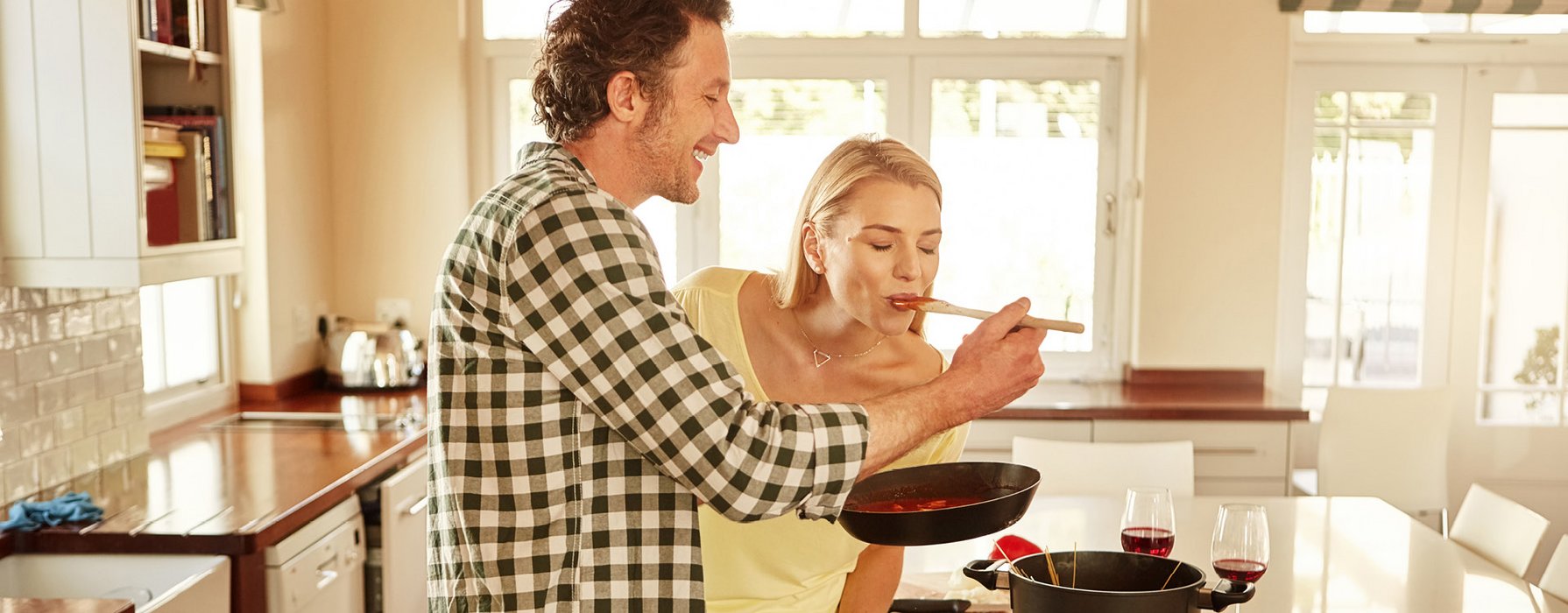 Paar in der Küche probiert aus einer Pfanne Tomatensauce mit dem Kochlöffel