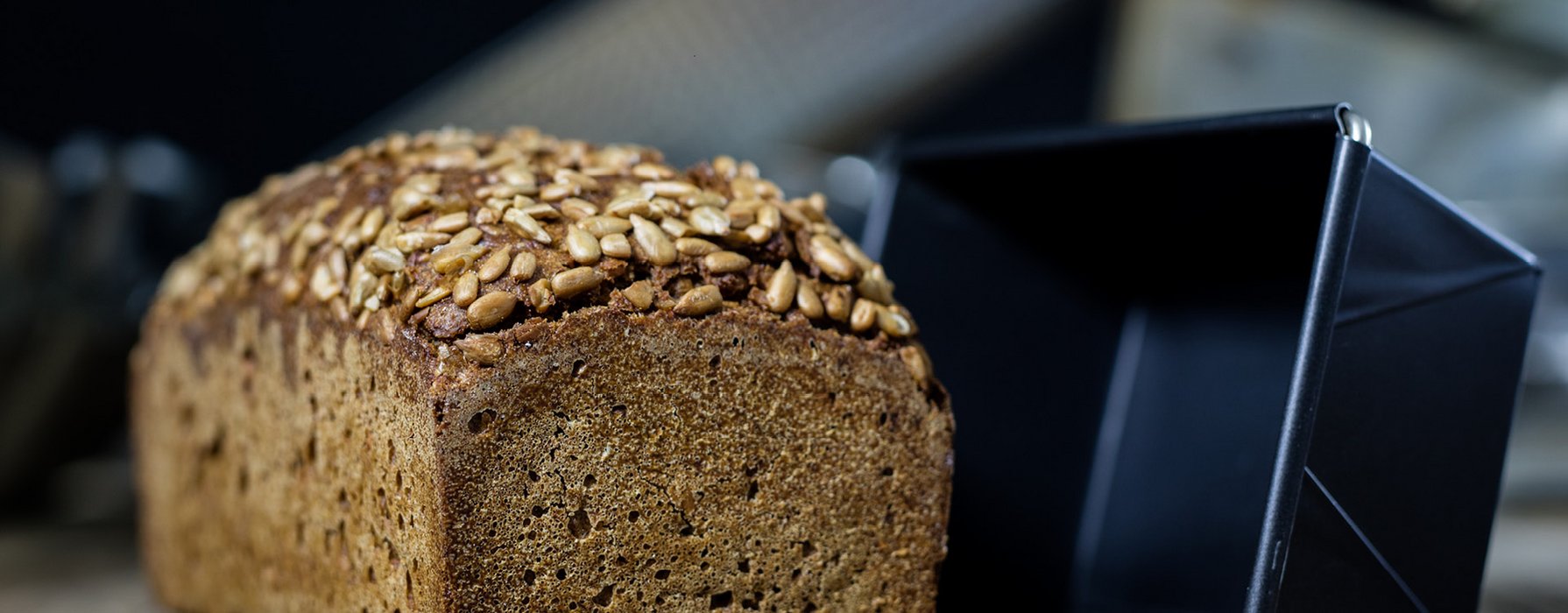 A baked loaf of bread is placed next to a black loaf pan