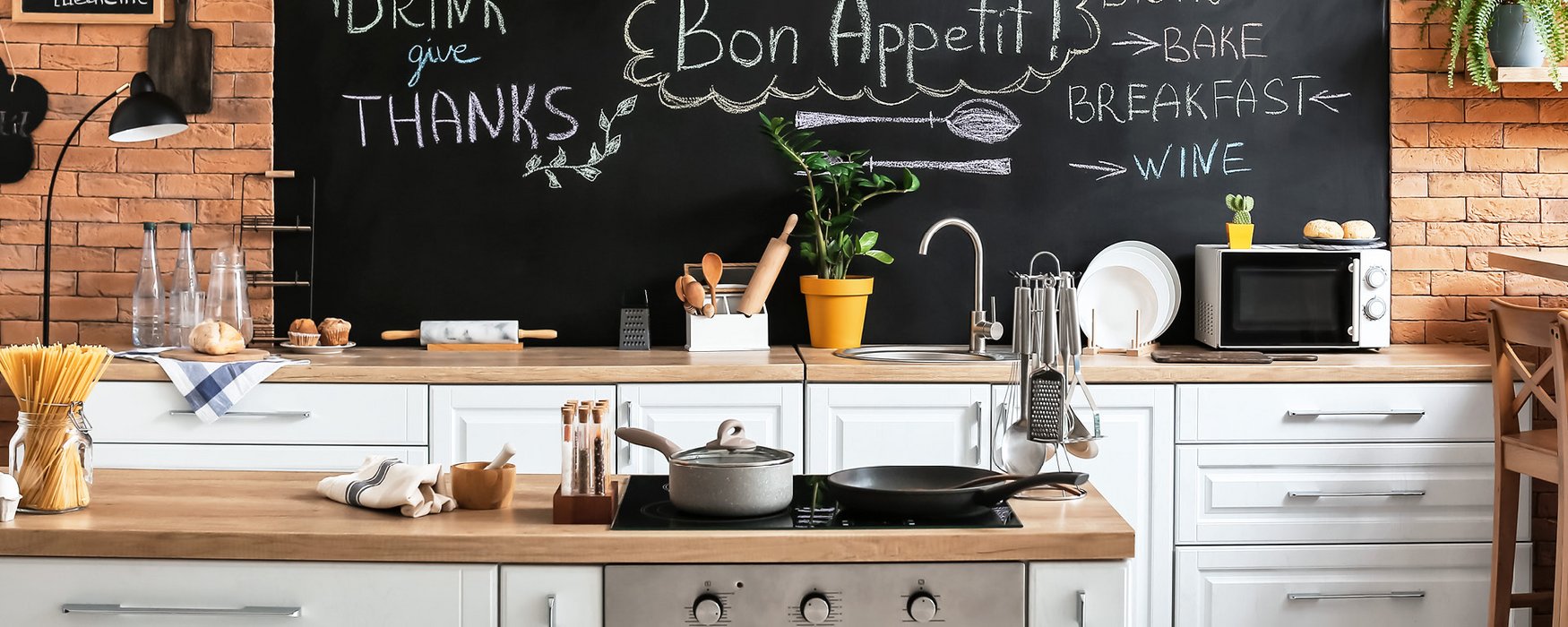 Kitchen unit with different cooking utensil and a chalkboard in the back with keywords to the topic of cooking