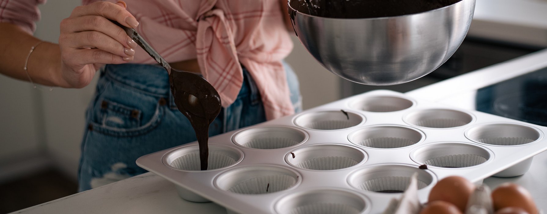 In eine silberne Muffinform wird mit einem Löffel dunkler Schokoladenteig eingefüllt