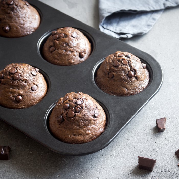 Muffin tray with baked chocolate muffins in it is standing on a table