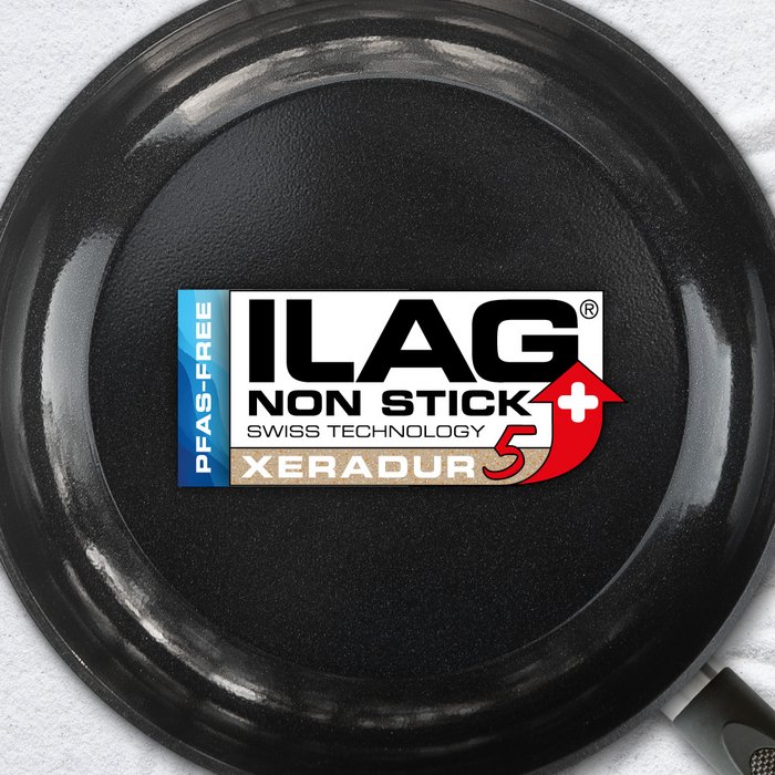 Black glossy inside of a frying pan - ILAG logo with beige shaded Xeradur 5 lettering in the center and on the left hand side an extra labeling "PFAS-FREE" in blue