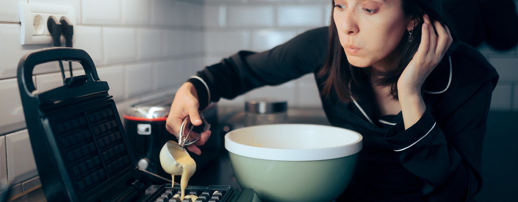 Young woman is filling some dough with an ice cream scoop into an waffle iron