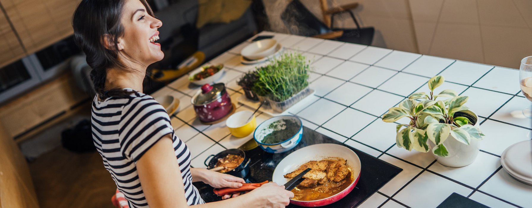 Happy young woman is roasting some chicken escalopes in a pan with white inside coating